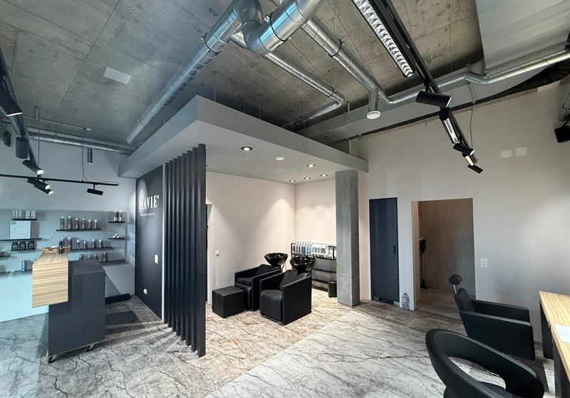 Blick durch den Salon auf die Sichtbetondecke mit Lüftungskanälen und schwarzen Lichtschienen